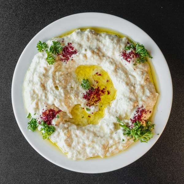 A white plate of creamy baba ghanoush topped with olive oil, parsley, and red spice.