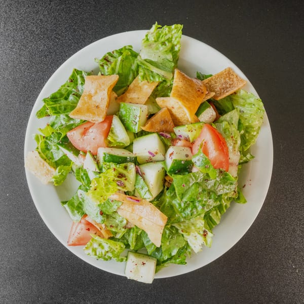 A vibrant fattoush salad with crisp lettuce, tomatoes, cucumbers, and toasted pita bread on a white plate.