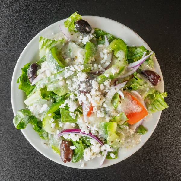 Overhead view of a Greek salad with lettuce, peppers, onions, olives, feta, and dressing.