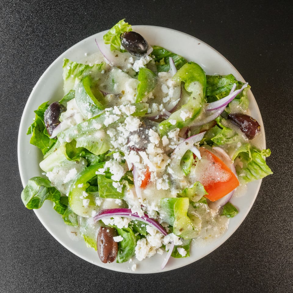Overhead view of a Greek salad with lettuce, peppers, onions, olives, feta, and dressing.