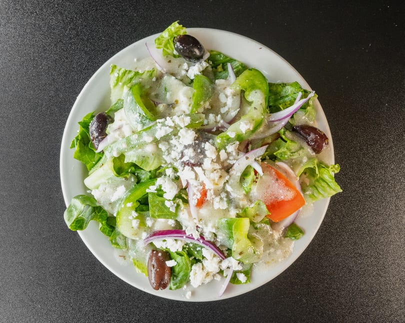 Overhead view of a Greek salad with lettuce, peppers, onions, olives, feta, and dressing.