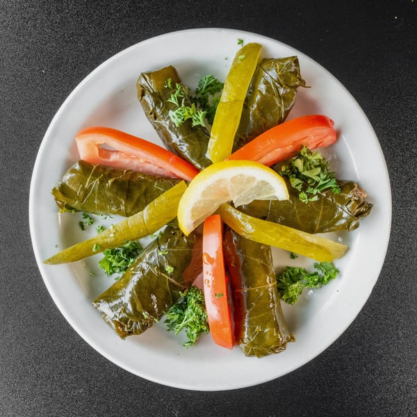 Grape leaves stuffed with rice and meat, garnished with lemon, tomatoes, pickles, and parsley.