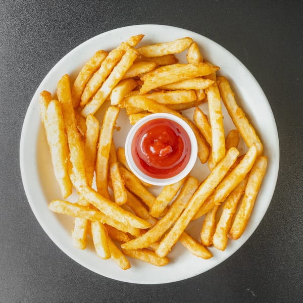 Golden french fries arranged on a white plate with a small cup of ketchup in the center.