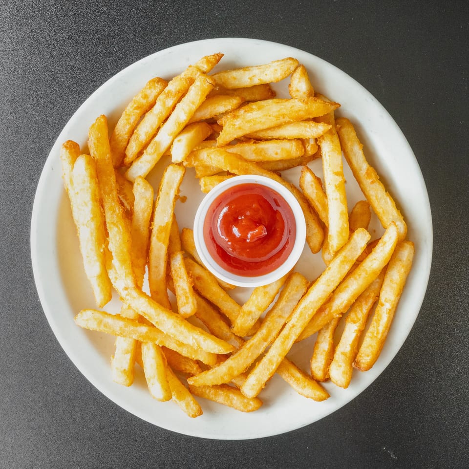 Golden french fries arranged on a white plate with a small cup of ketchup in the center.