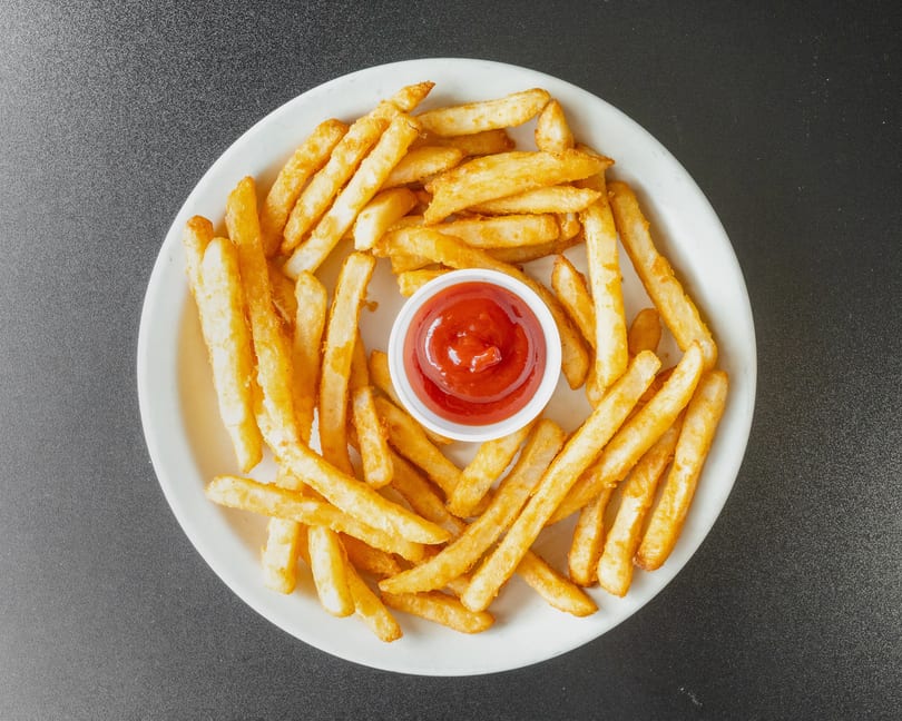 Golden french fries arranged on a white plate with a small cup of ketchup in the center.