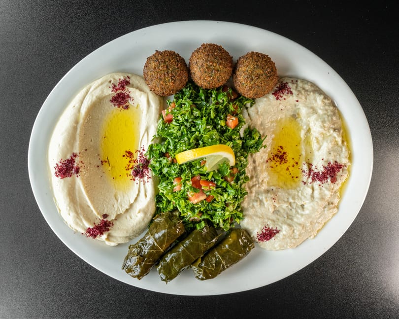 A platter with hummus, baba ghanoush, falafel, tabbouleh, and stuffed grape leaves.