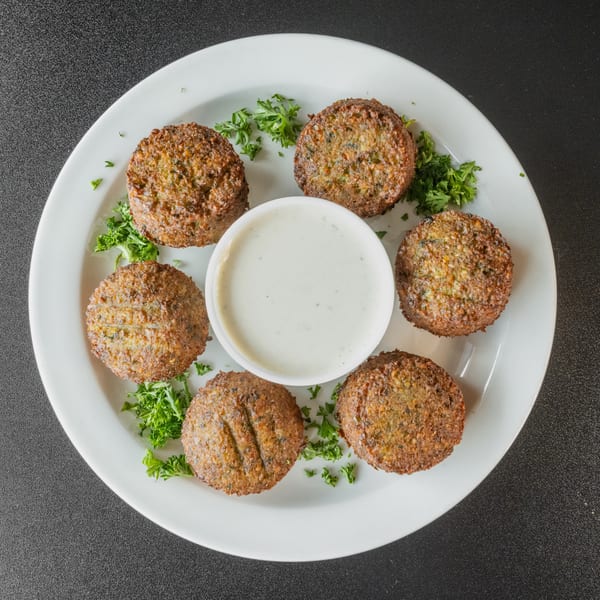 Six golden-brown falafel patties arranged around a white bowl of creamy sauce on a white plate.
