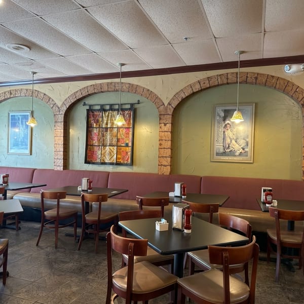 Empty restaurant dining room with booths, tables, chairs, and arched wall decor.