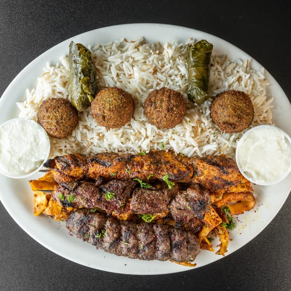 A large platter of Middle Eastern food with rice, falafel, stuffed grape leaves, and various kebabs.