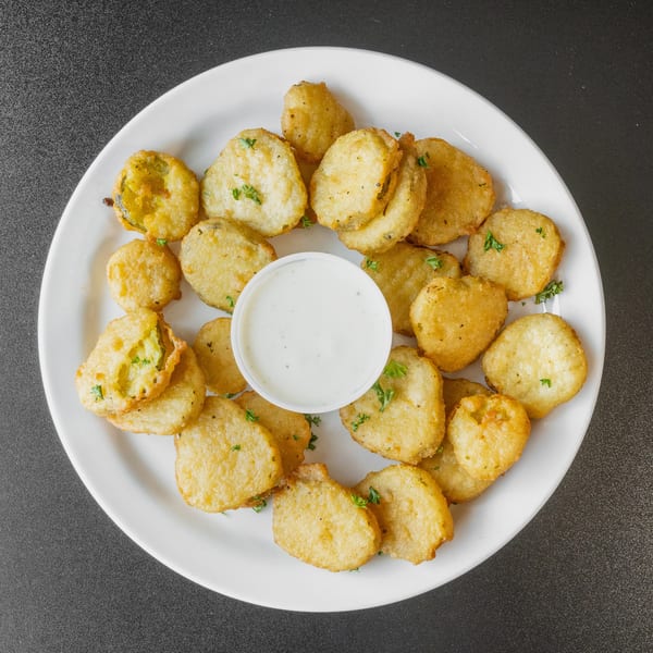 Golden-brown fried pickle slices with a side of ranch dressing on a white plate.