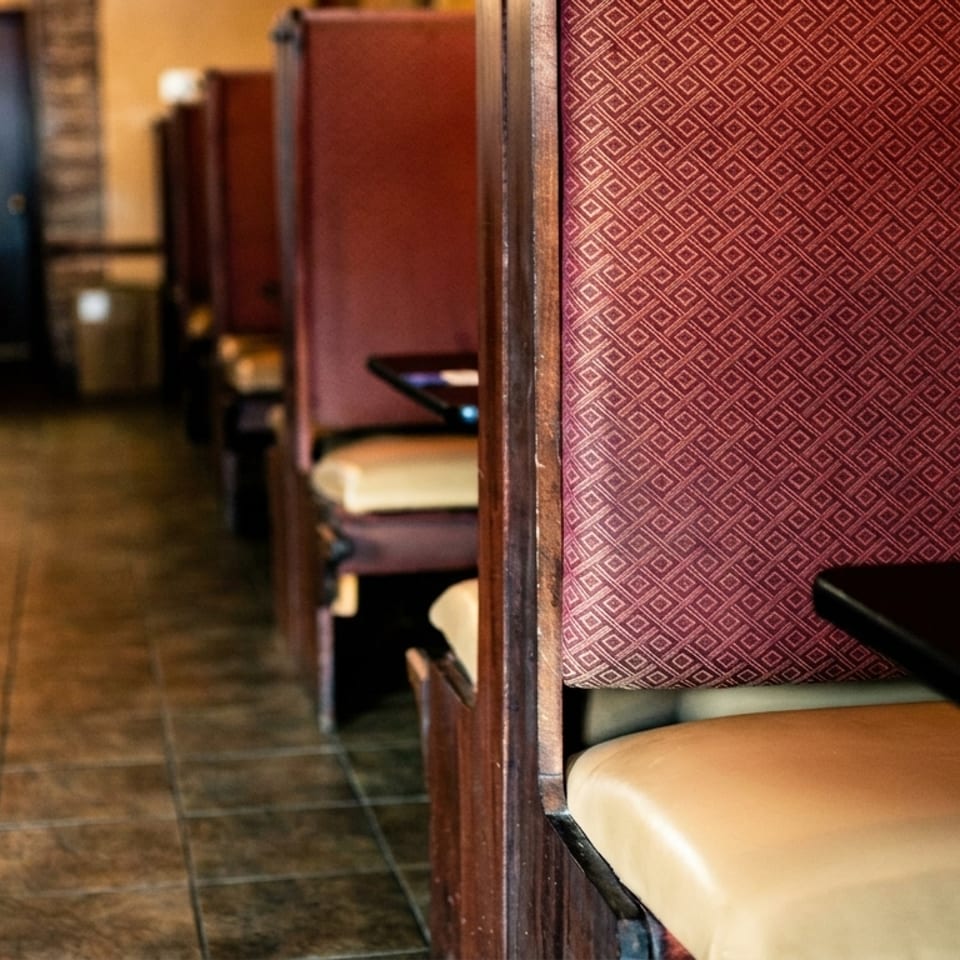 A row of empty restaurant booths with red patterned backs and tan seats, leading to a dark doorway.